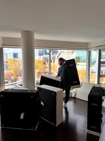 A mover carrying furniture through a condo with a view of the Toronto skyline