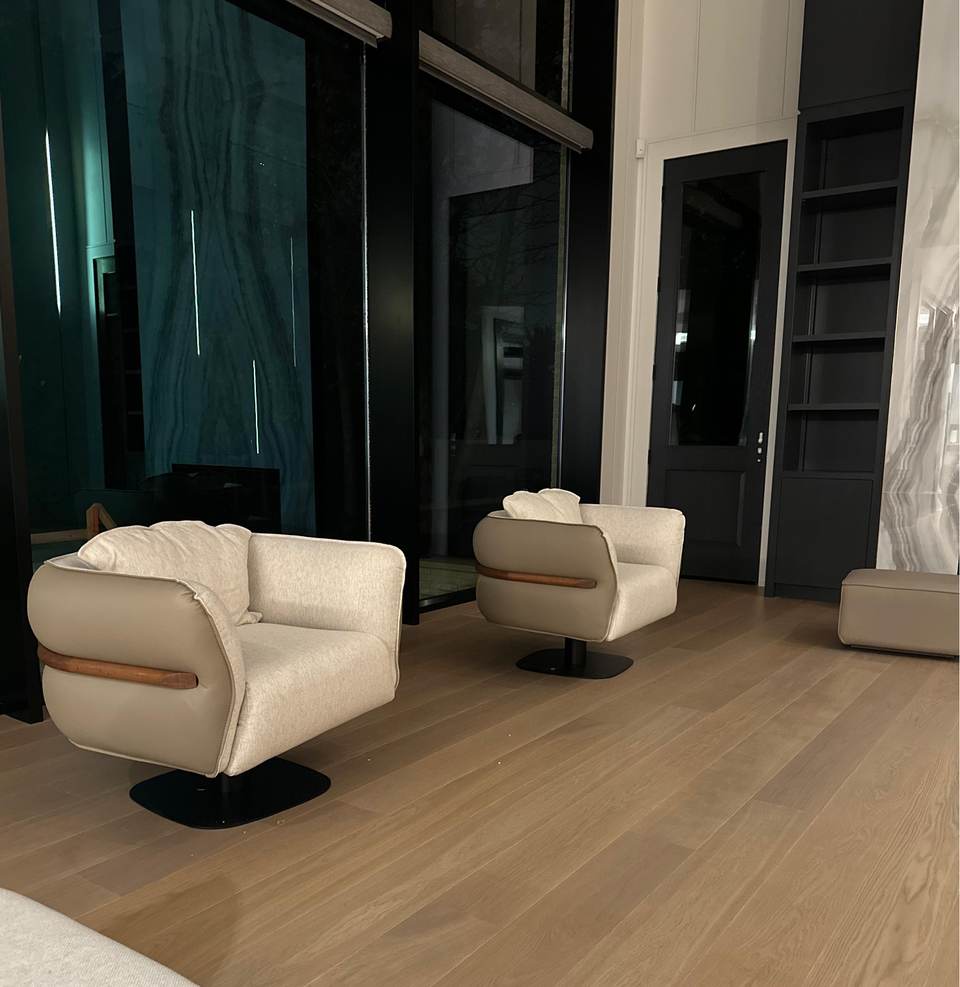 Two cream swivel armchairs placed on a wide-plank floor in a dark-panelled room of a North York home