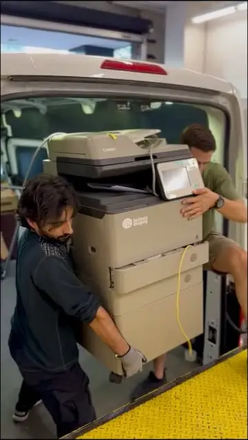 Two movers lifting an office copier off the back of a van